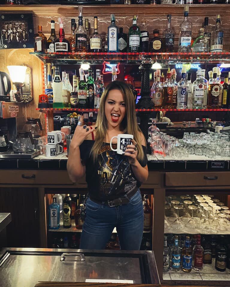 A bartender behind the bar holding a 4th Street Bar mug
